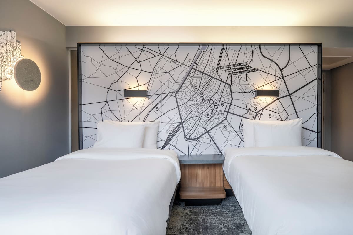 A modern hotel room with two beds, a large wall map, and a unique light fixture.