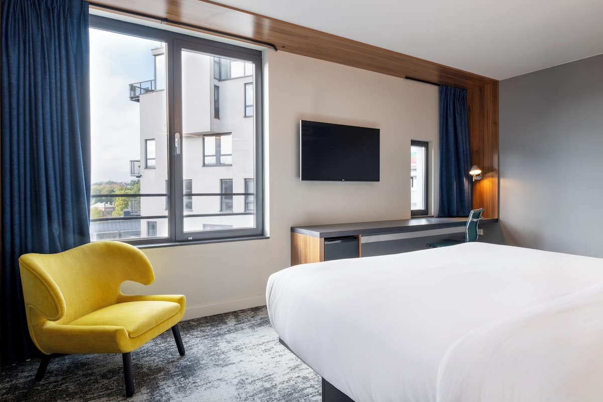A hotel room with a bed, a desk, a chair, a TV, and a window with curtains.
