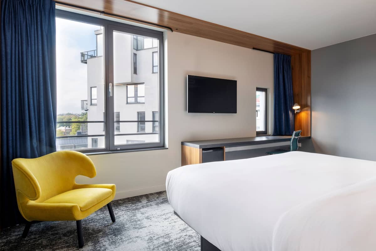 A hotel room with a bed, a desk, a chair, a TV, and a window with curtains.