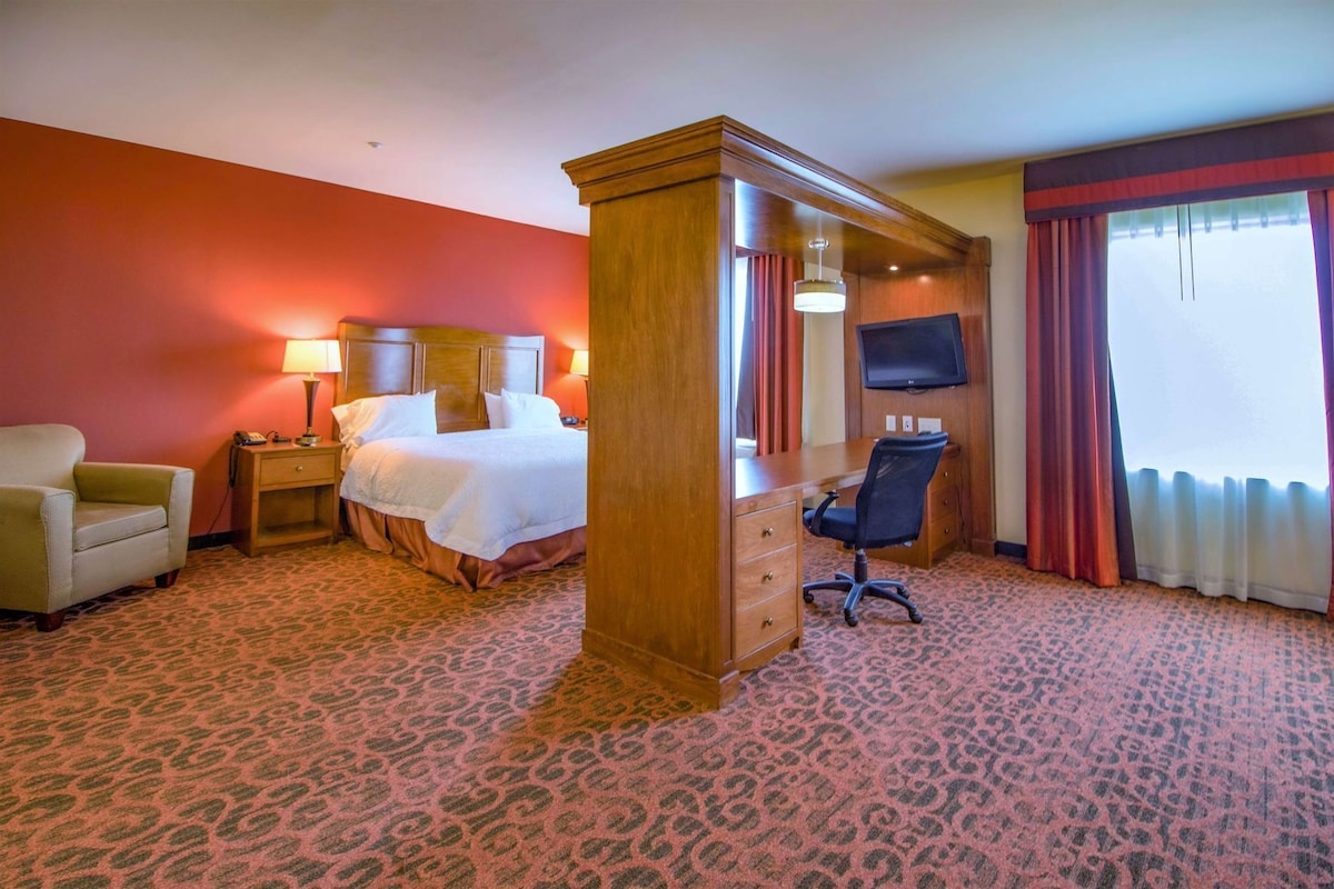 A hotel room with a bed, a desk, a chair, a TV, and a window with curtains.