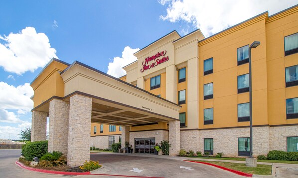 Ein Hampton Inn & Suites Hotel mit Natursteinfassade, zahlreichen Fenstern und blauem Himmel.