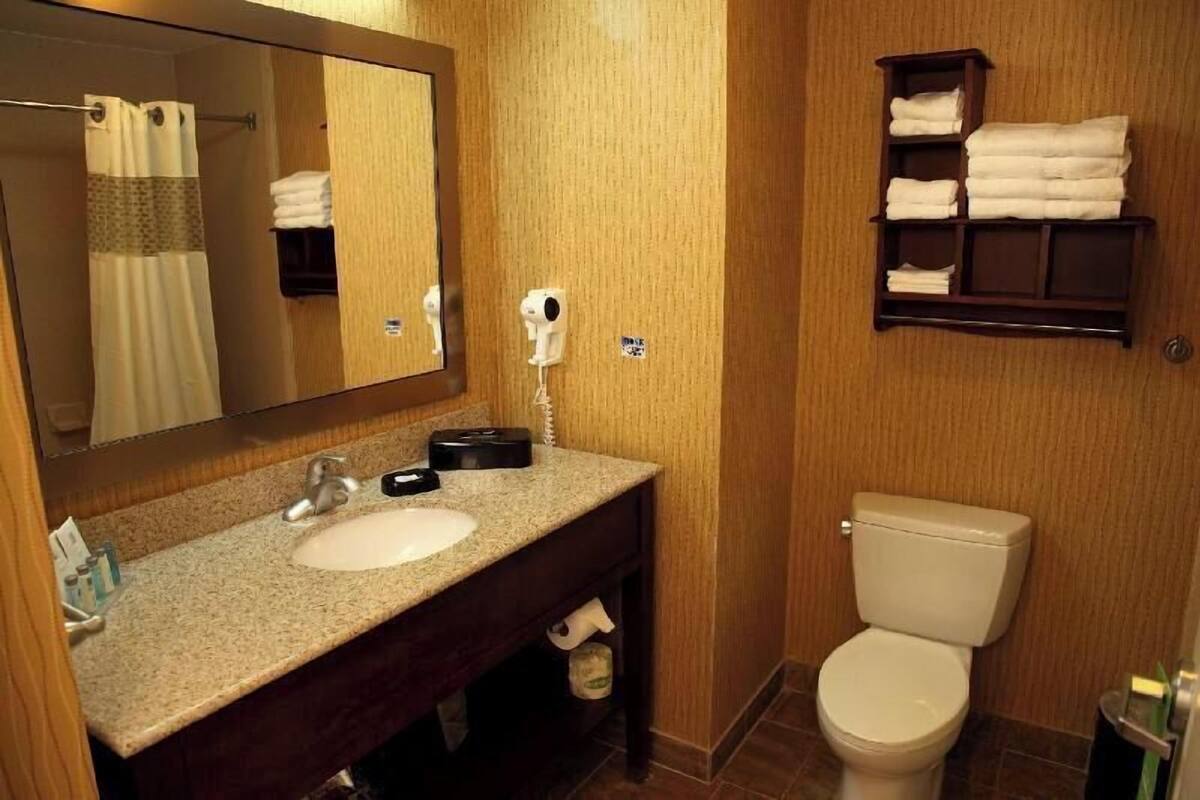 Un baño con lavamanos, espejo, toallero y retrete.