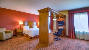Ein Hotelzimmer mit Bett, Schreibtisch, Stuhl, Nachttisch, Fernseher und einem Fenster mit Vorhängen.
