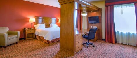 A hotel room with a bed, a desk, a chair, a nightstand, a television, and a window with curtains.
