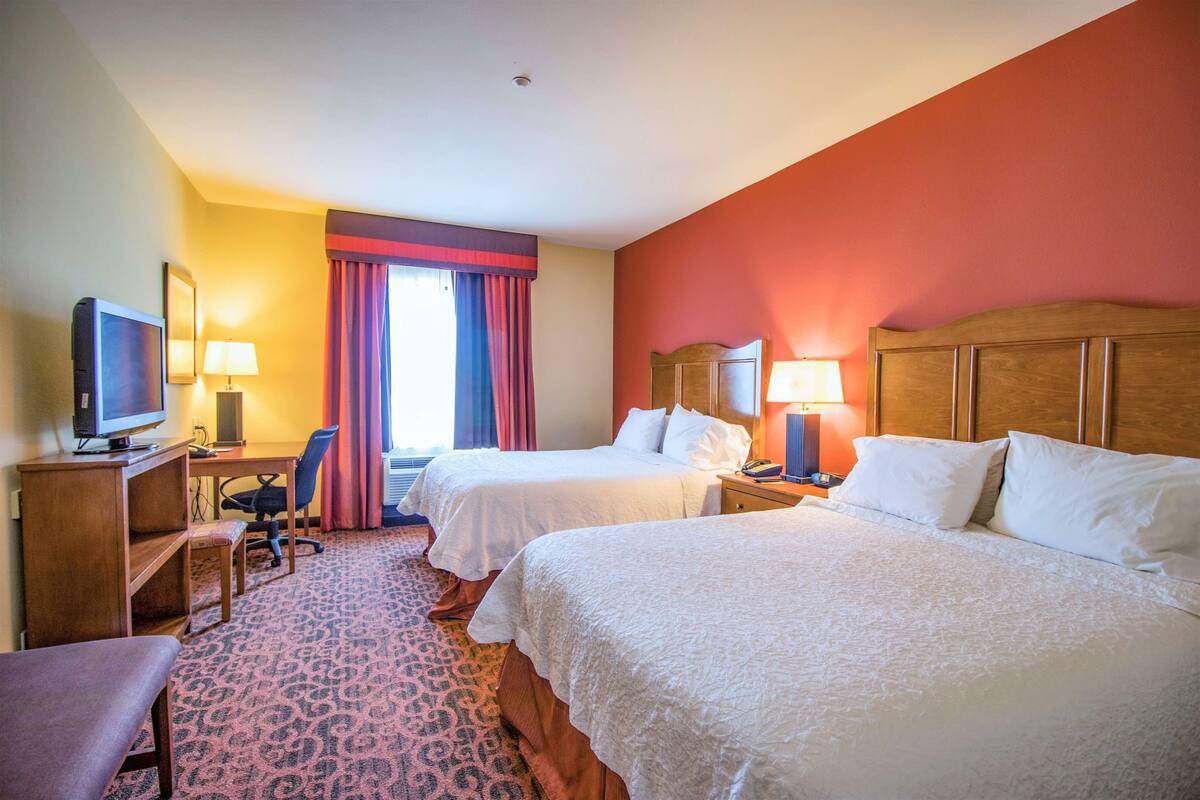 Habitación de hotel con dos camas, un escritorio con computadora, un televisor y una silla.