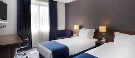 A hotel room with two beds, a desk, a chair, a television, and a window with curtains.