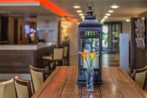 Una mesa de madera con un florero de vidrio, flores y un farol decorativo.
