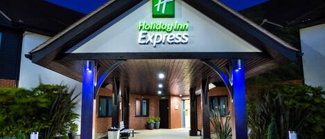 L’entrée d’un bâtiment Holiday Inn Express, avec une allée couverte, des plantes en pot et un banc.