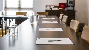 A conference room with a long table, chairs, a projector, and a cabinet with office supplies. - Holiday Inn Express Colchester by IHG (Colchester)