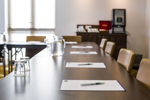 A conference room with a long table, chairs, a projector, and a cabinet with office supplies. - Holiday Inn Express Colchester by IHG (Colchester)