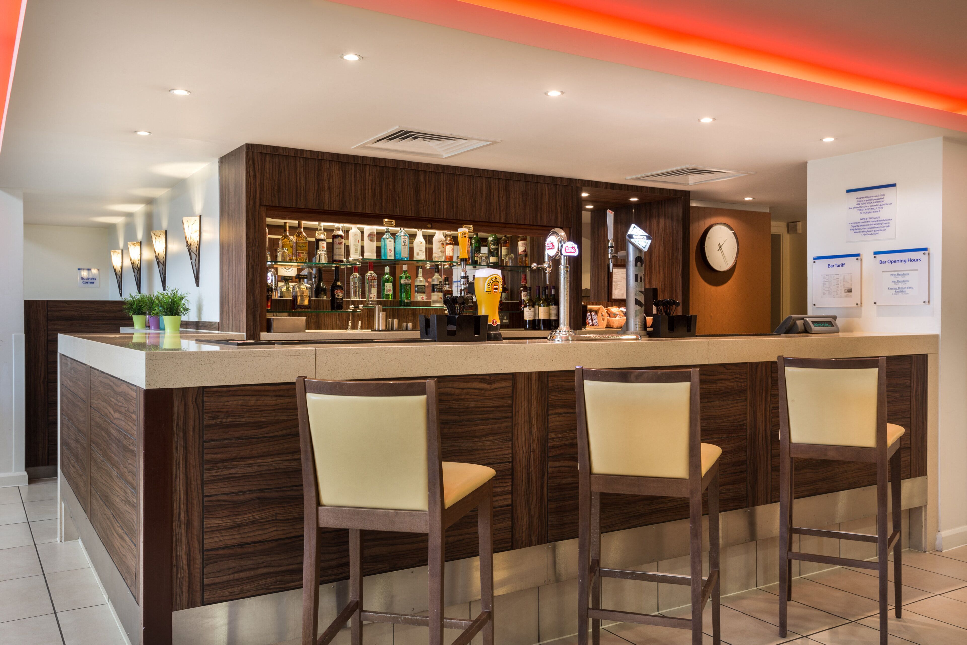 Zona de bar con mostrador de madera, varias botellas de licor y un reloj en la pared.