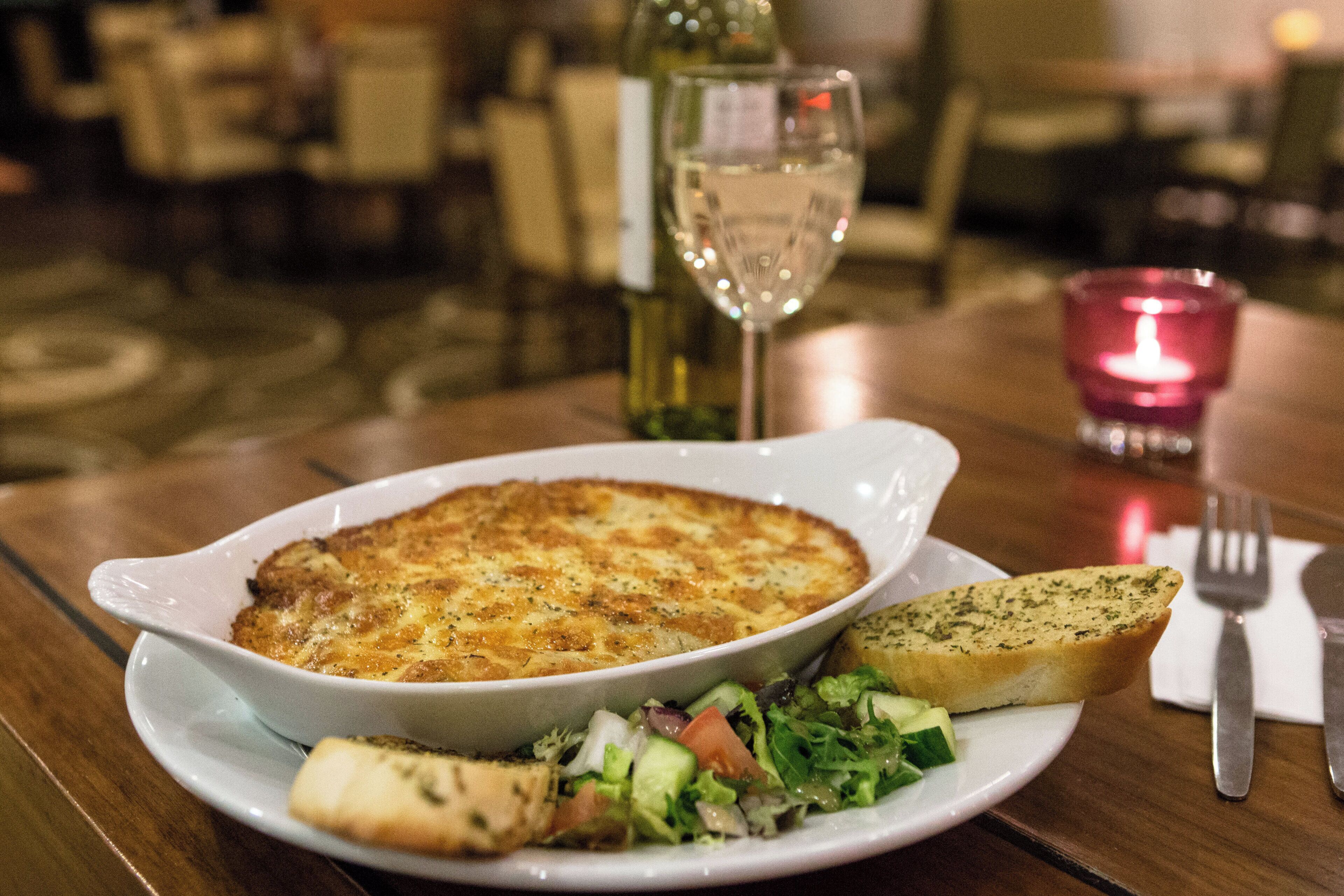 A plate with a baked dish, a slice of bread, and a salad on a table.