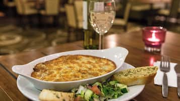 A plate with a baked dish, a slice of bread, and a salad on a table.