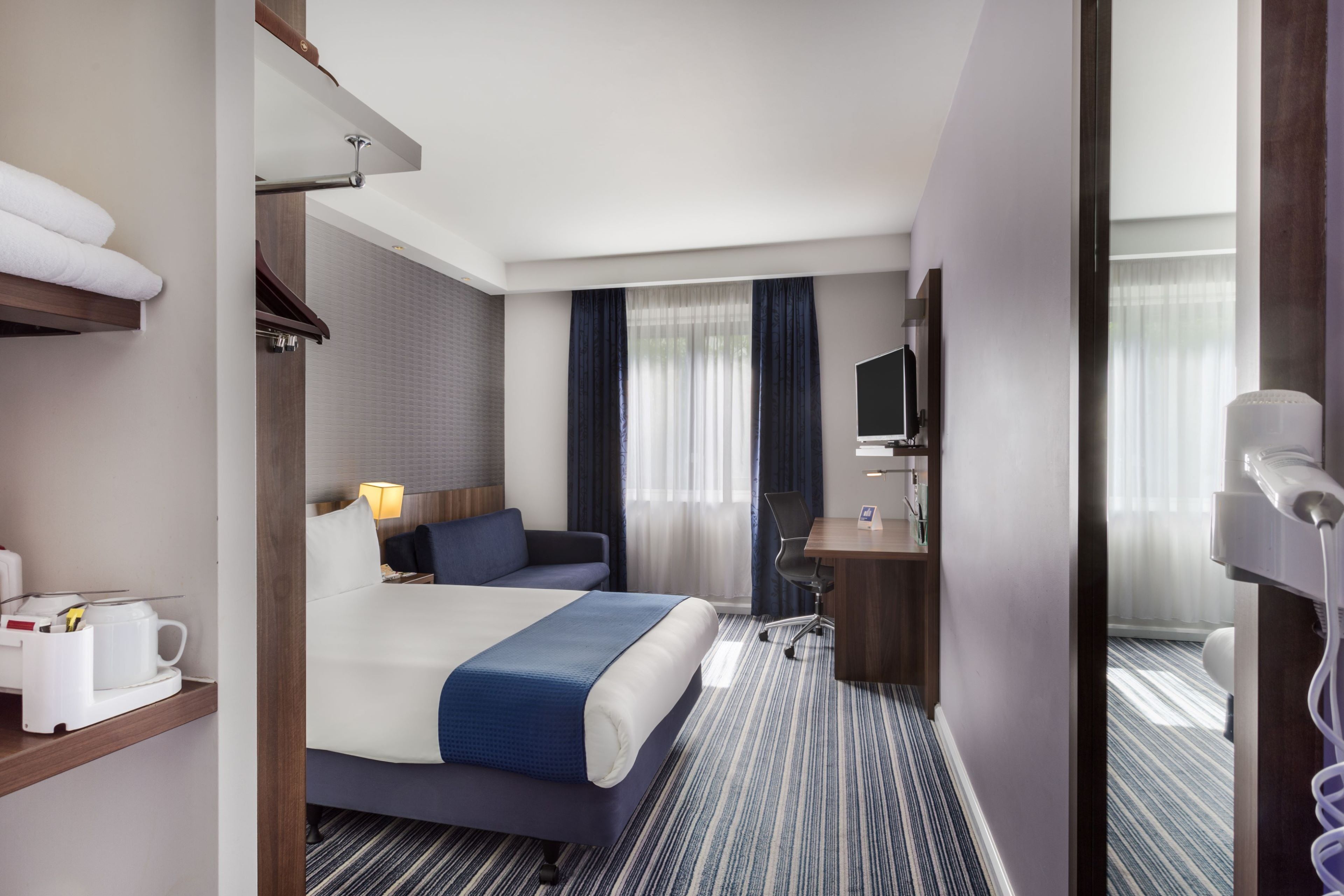A hotel room with a bed, a desk, a chair, a TV, and a bathroom.