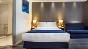 A hotel room with a large bed, a chair, a nightstand with a lamp, and a painting on the wall. - Holiday Inn Express Colchester by IHG (Colchester)