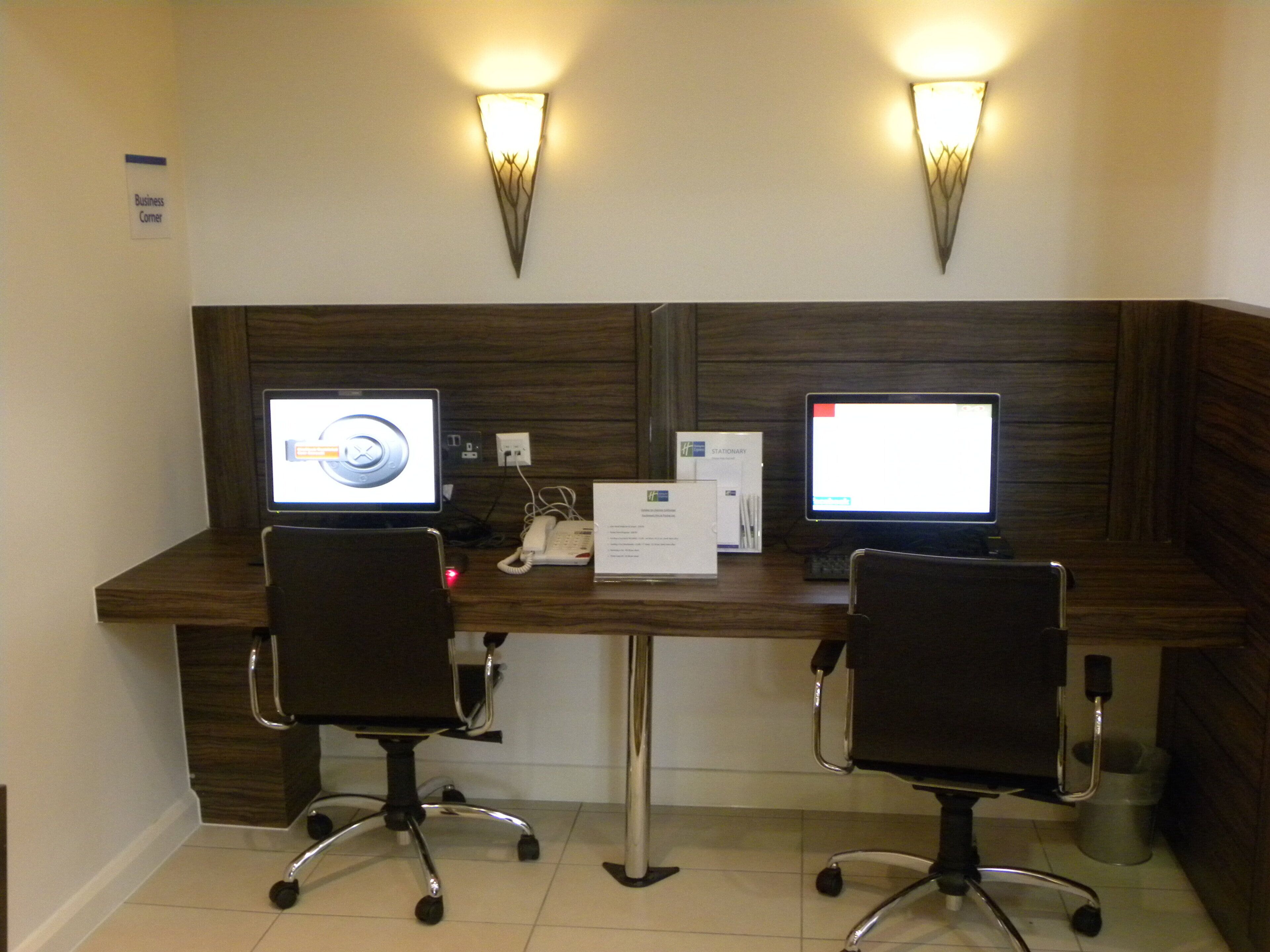 Een werkruimte met twee bureaus, elk met een computerscherm, een telefoon en een bordje met de tekst 'business corner'.