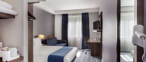 A hotel room with a bed, a desk, a chair, a TV, and a hairdryer.