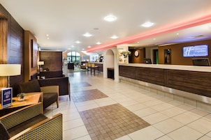 A hotel lobby with a reception desk, seating area, and a view of the dining area.