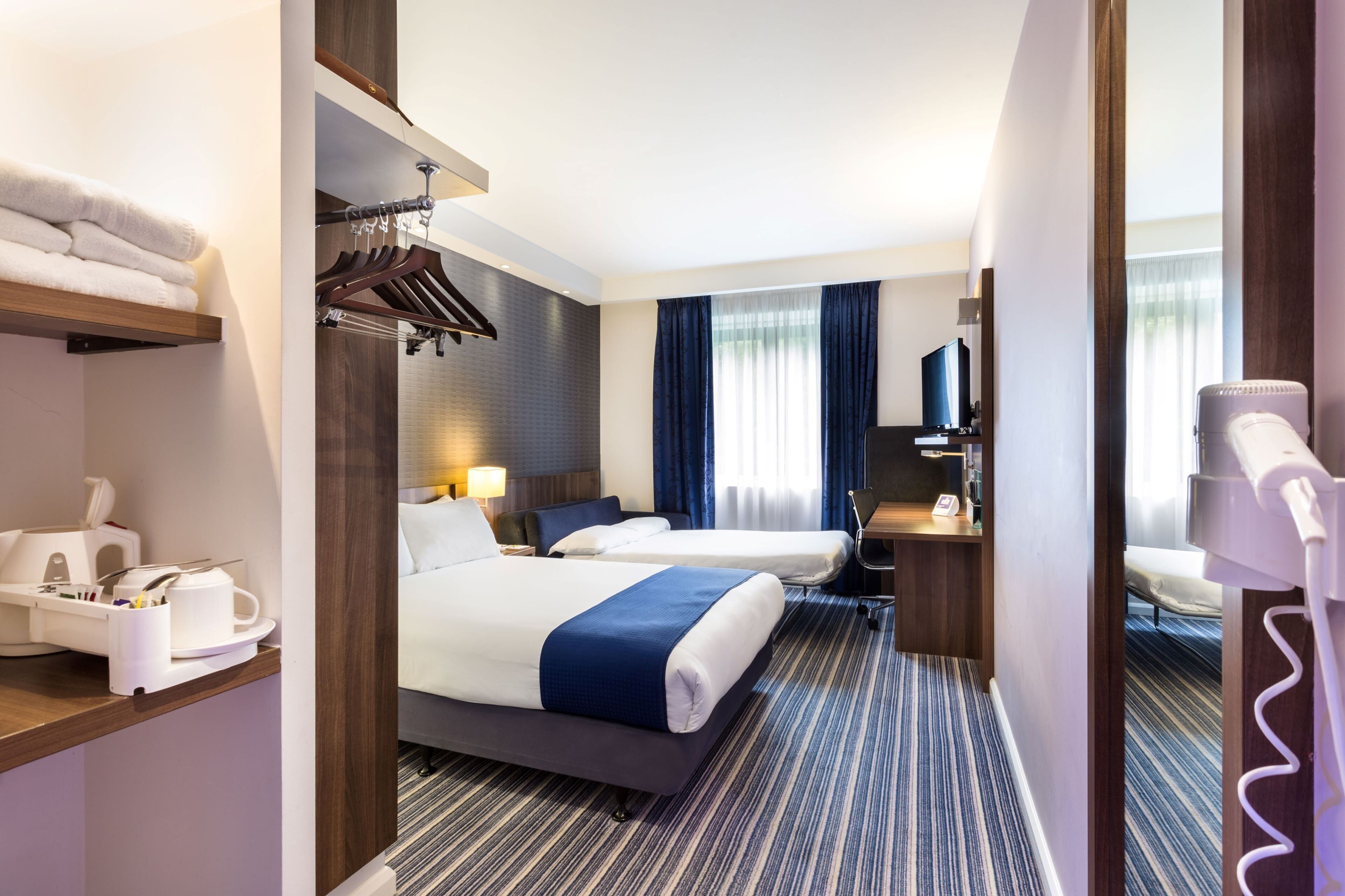 A hotel room with a bed, bedside table, lamp, and a mirror.
