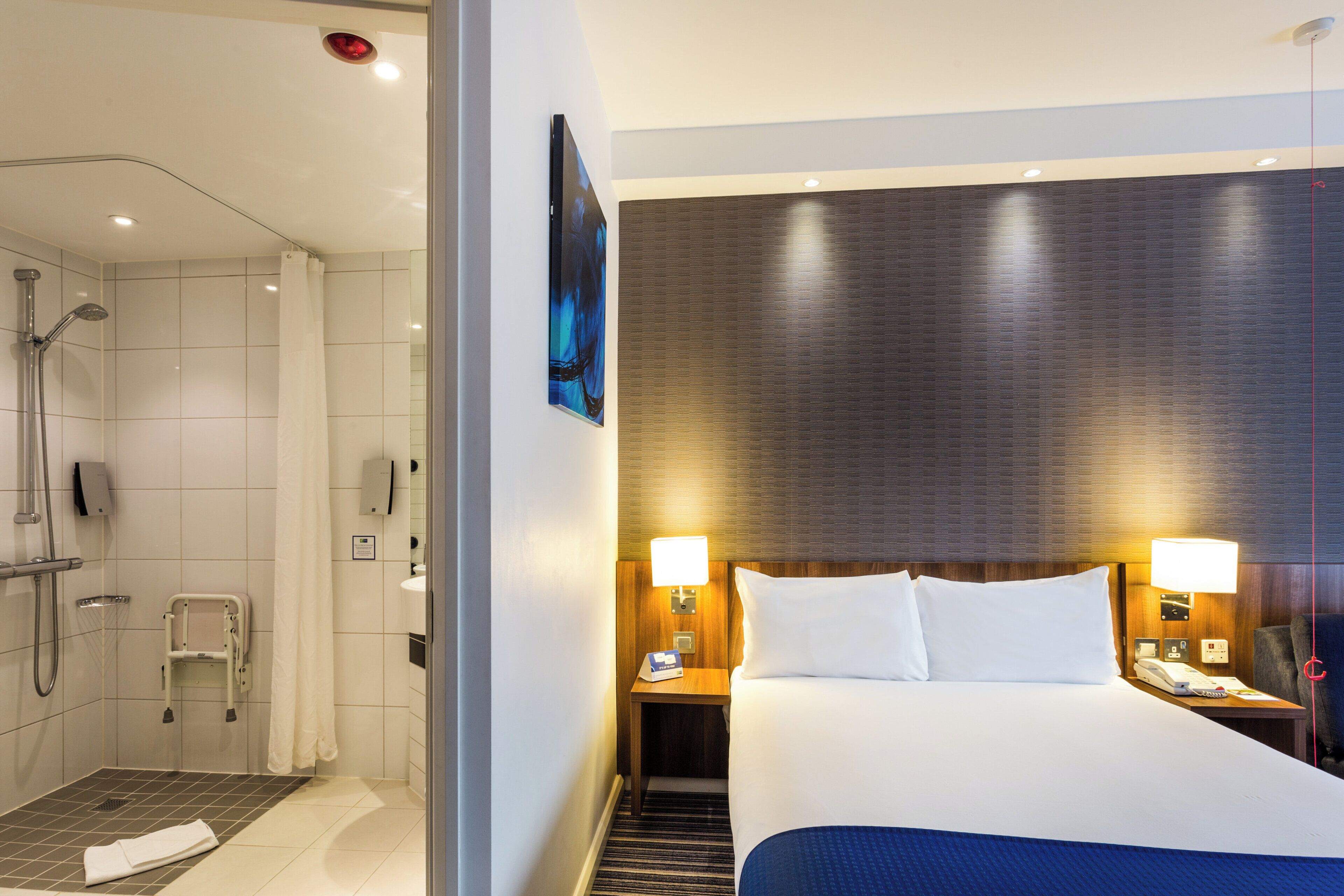 A hotel room with a shower, a bed, two bedside lamps, and a nightstand with a phone.
