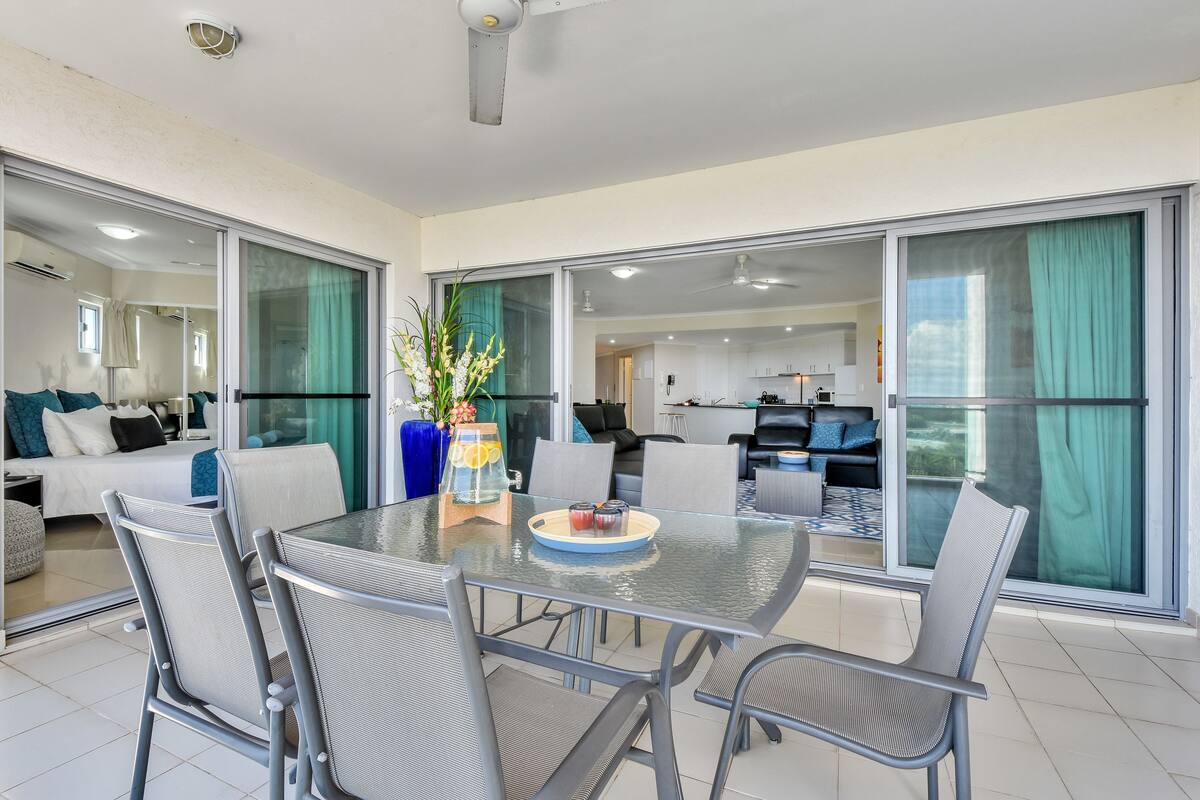 A modern living room with a glass dining table, grey chairs, and a sofa.