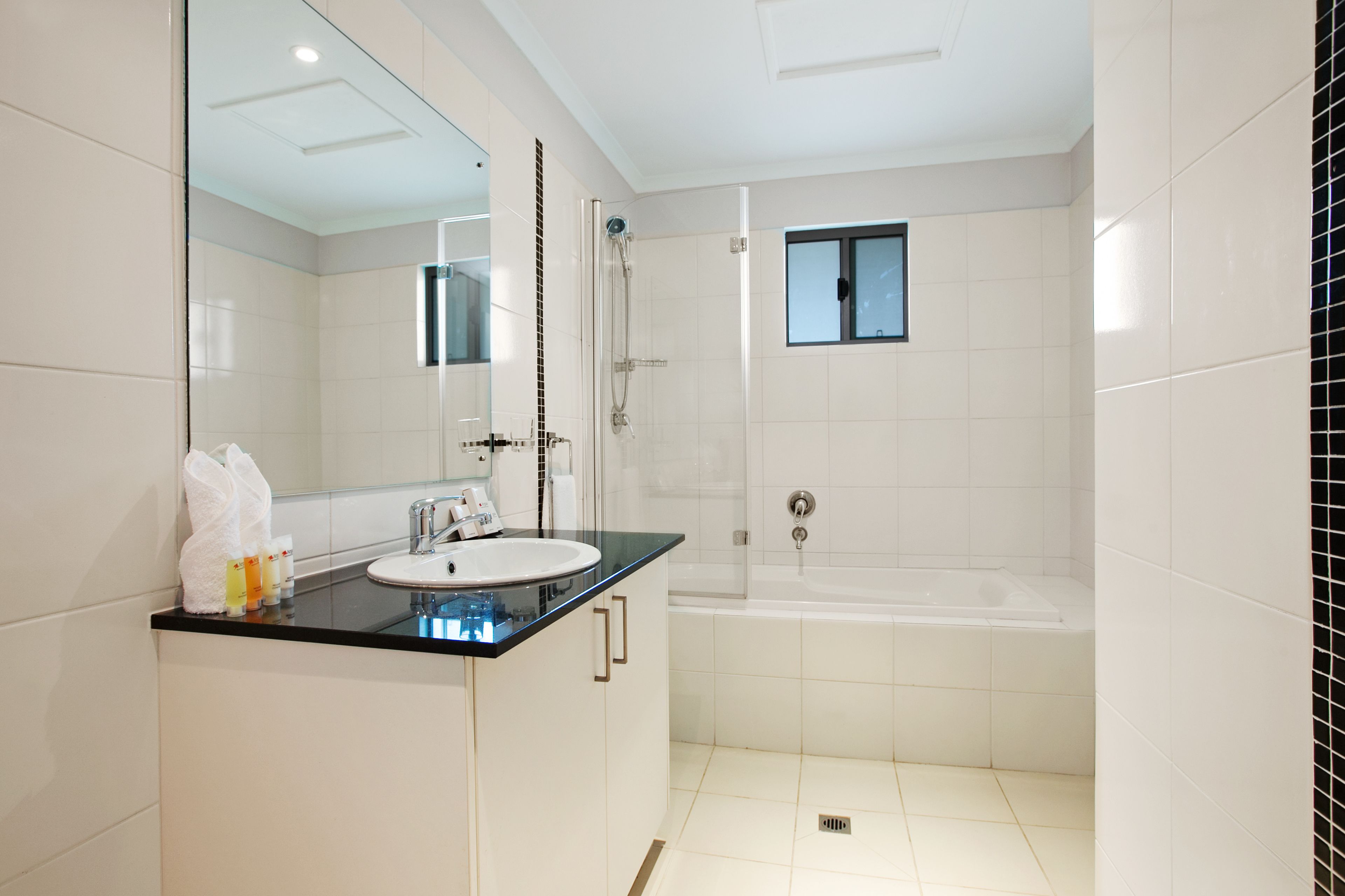 Une salle de bain moderne avec une douche à parois de verre, un lavabo blanc doté d’un plan de toilette noir et un grand miroir.