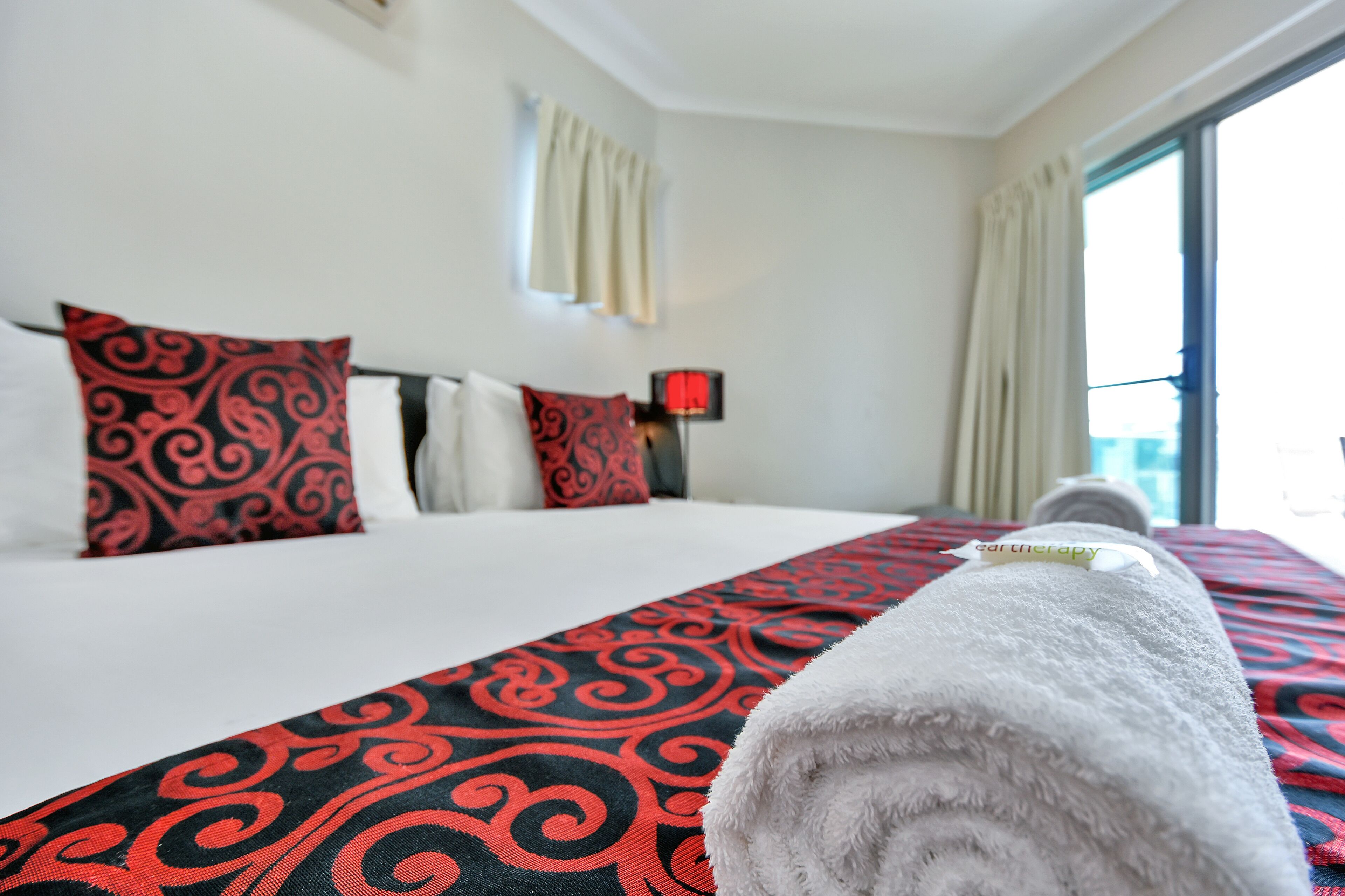 Una habitación de hotel con una cama, una colcha de cuadros roja y negra, y una toalla blanca sobre la cama.