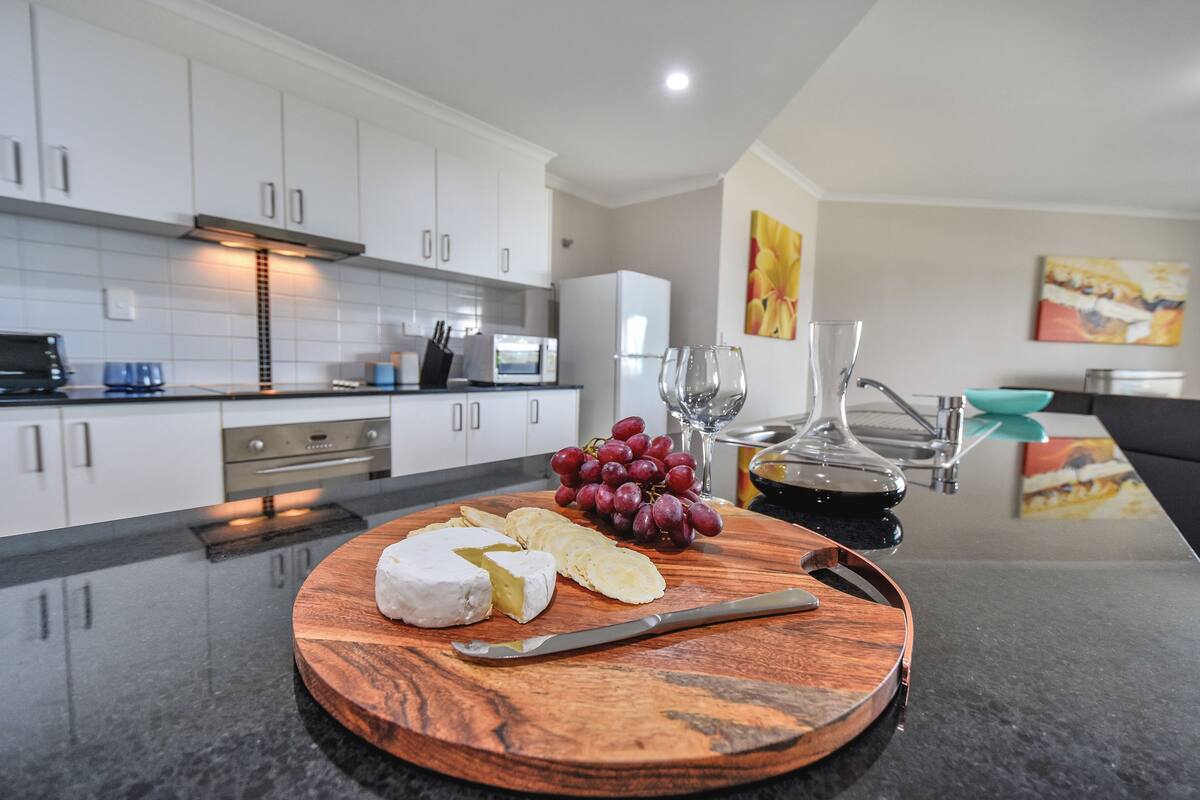 A modern kitchen with white cabinets, a wooden cutting board with cheese and grapes, and a knife.