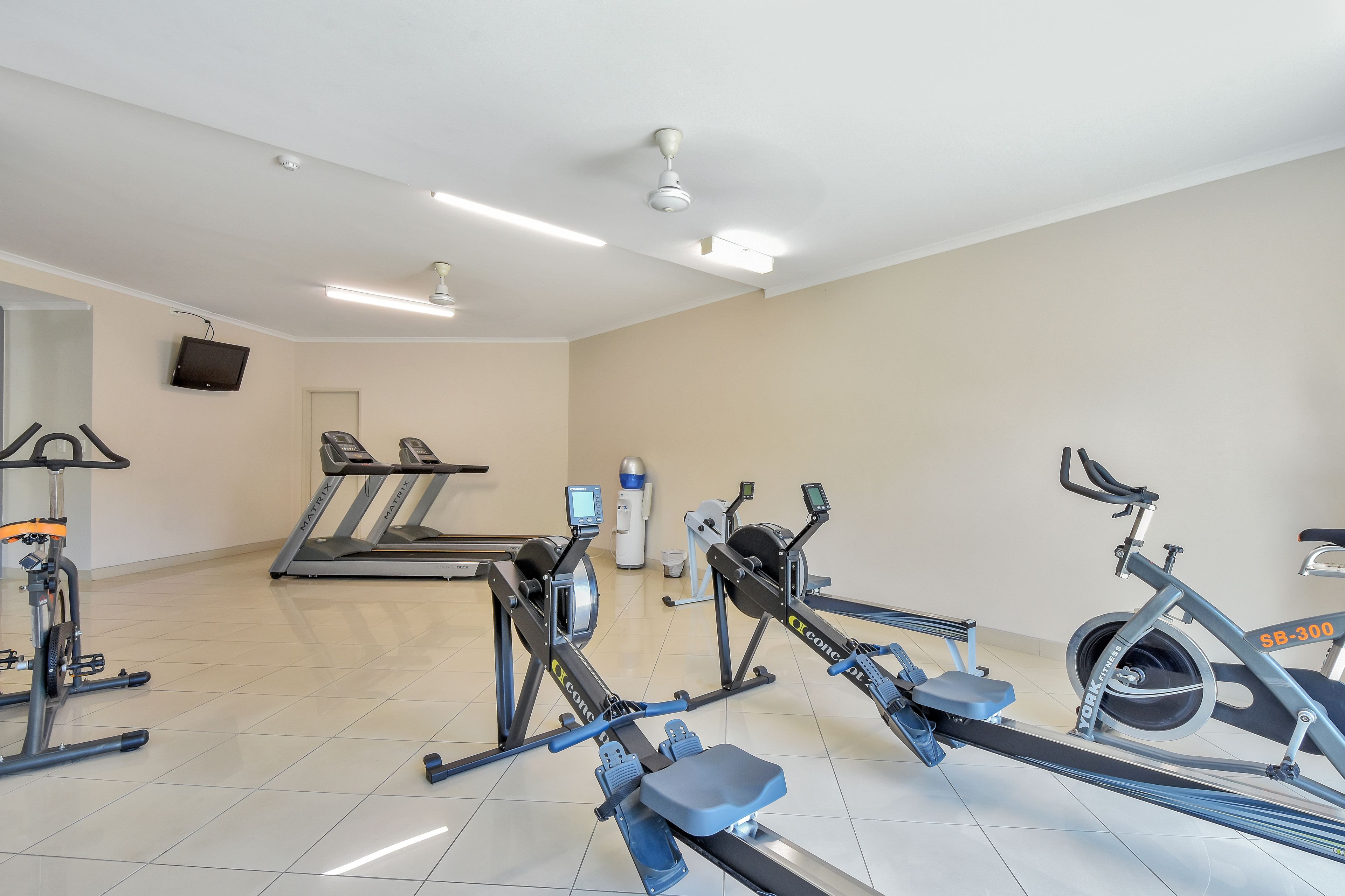 Une salle de sport équipée de divers appareils, notamment des tapis de course, des vélos d’appartement et un rameur.