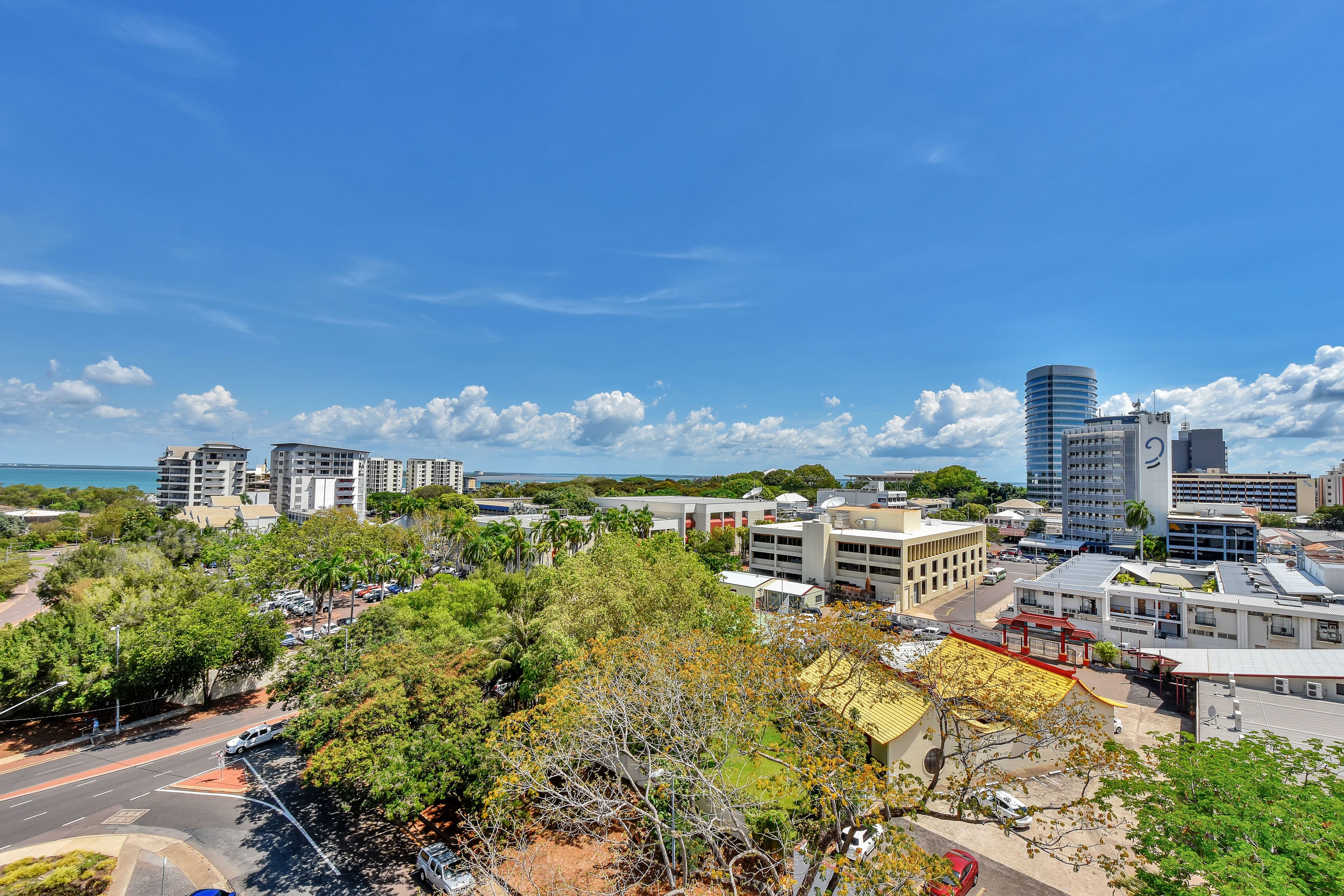 A cityscape with modern buildings, a road, and a body of water in the distance.