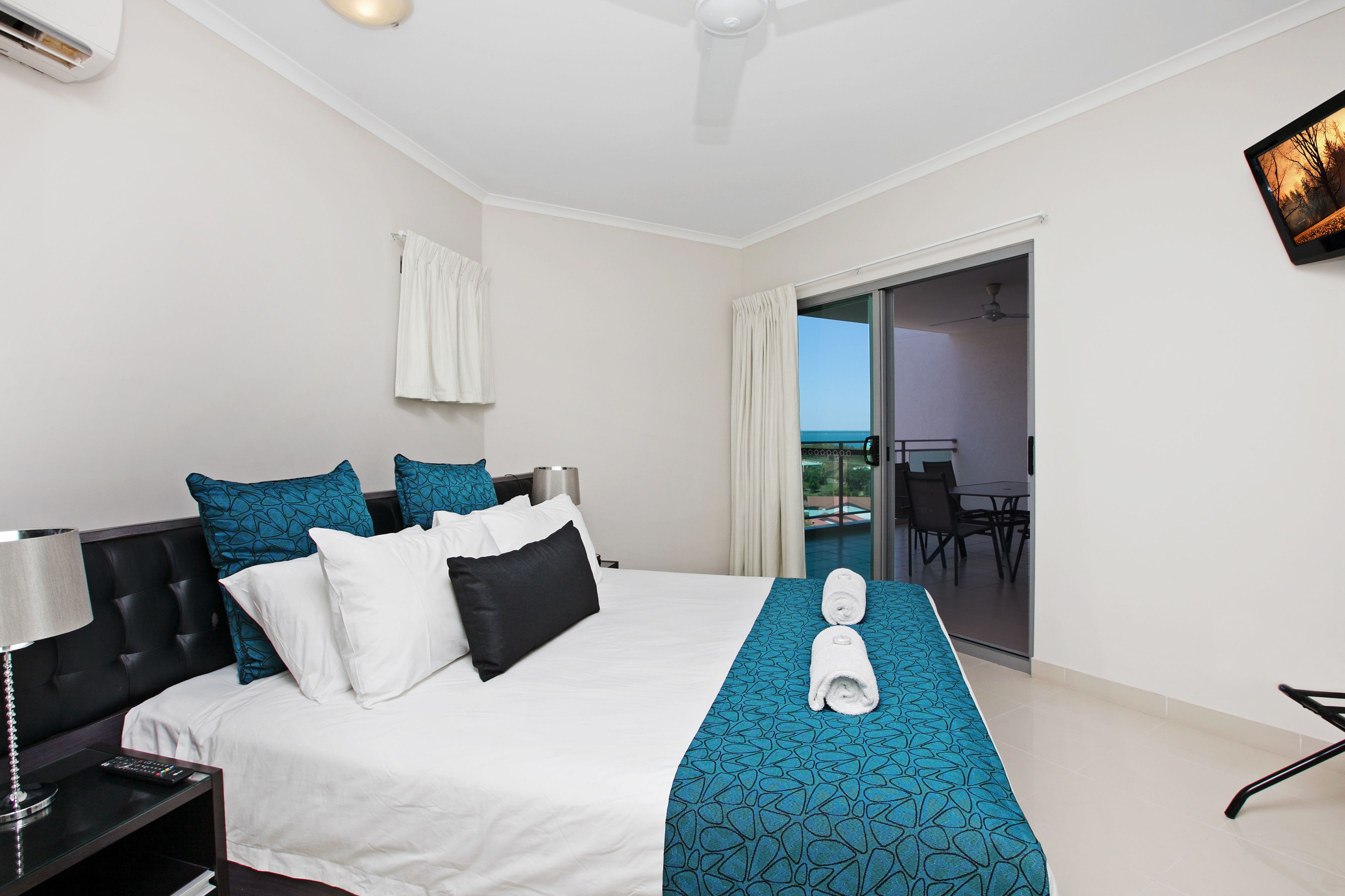 A hotel room with a large bed, a balcony with a view, and a dining area.