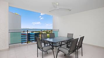 Un balcon avec une balustrade en verre, une table avec des chaises et un ventilateur de plafond.