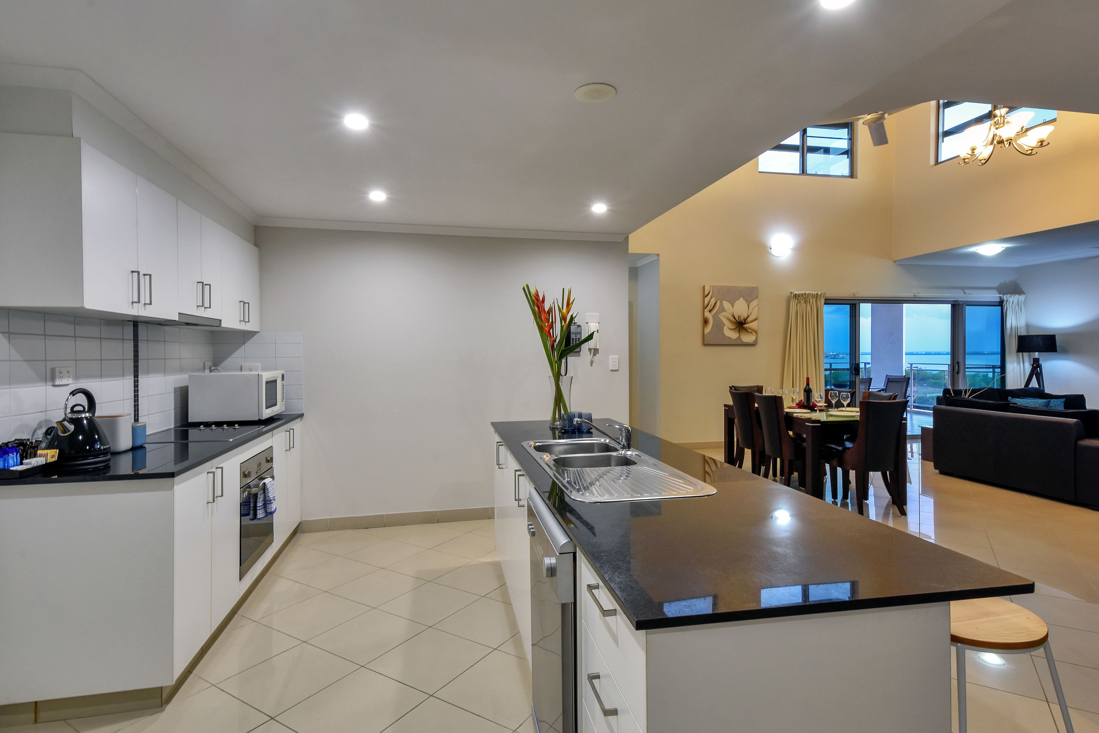 A modern kitchen with a central island, white cabinetry, and a dining area with a view.