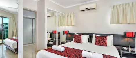 A hotel room with a large bed, a bedside table with a lamp, a mirror, and an air conditioning unit on the wall.