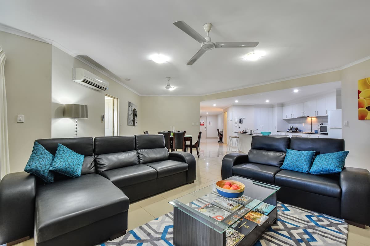 A modern living room with two black leather sofas, a glass coffee table, and a patterned rug.