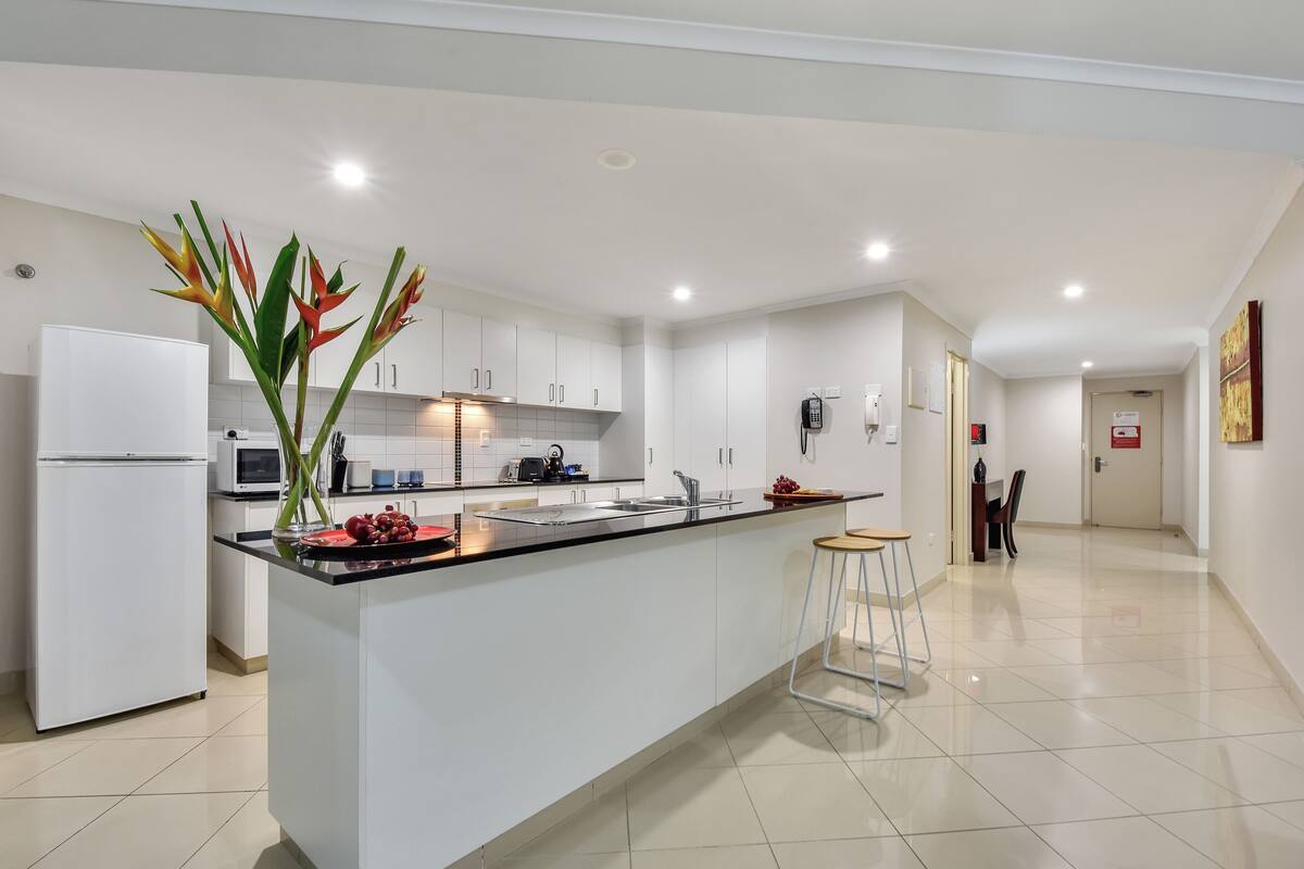 A modern kitchen with white cabinets, a black countertop, and a central island. There is a refrigerator, microwave, and a sink with a faucet.