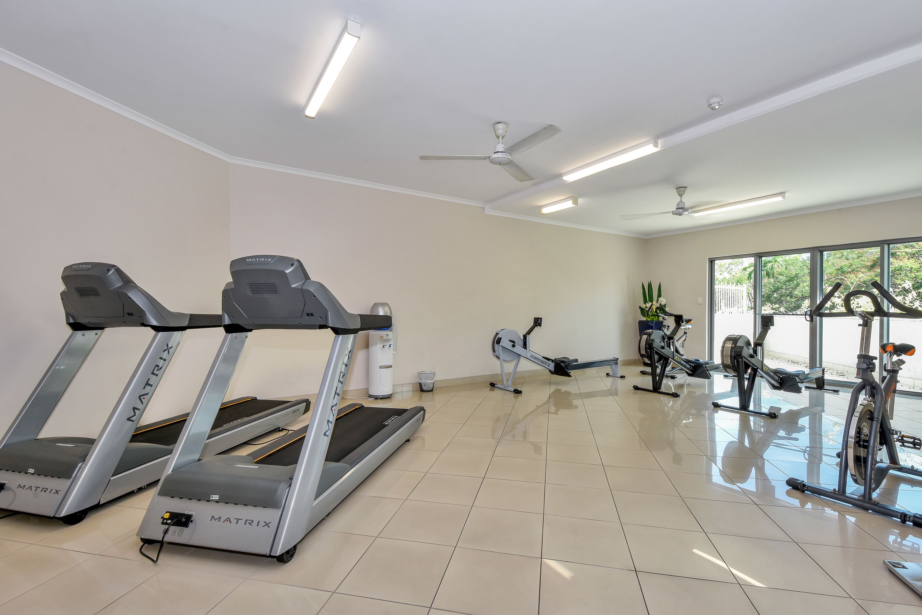 A gym with treadmills, stationary bikes, and ceiling fans.