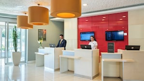 A hotel reception area with three reception desks, a large screen, and a potted plant. - ibis Kayseri (Kocasinan)