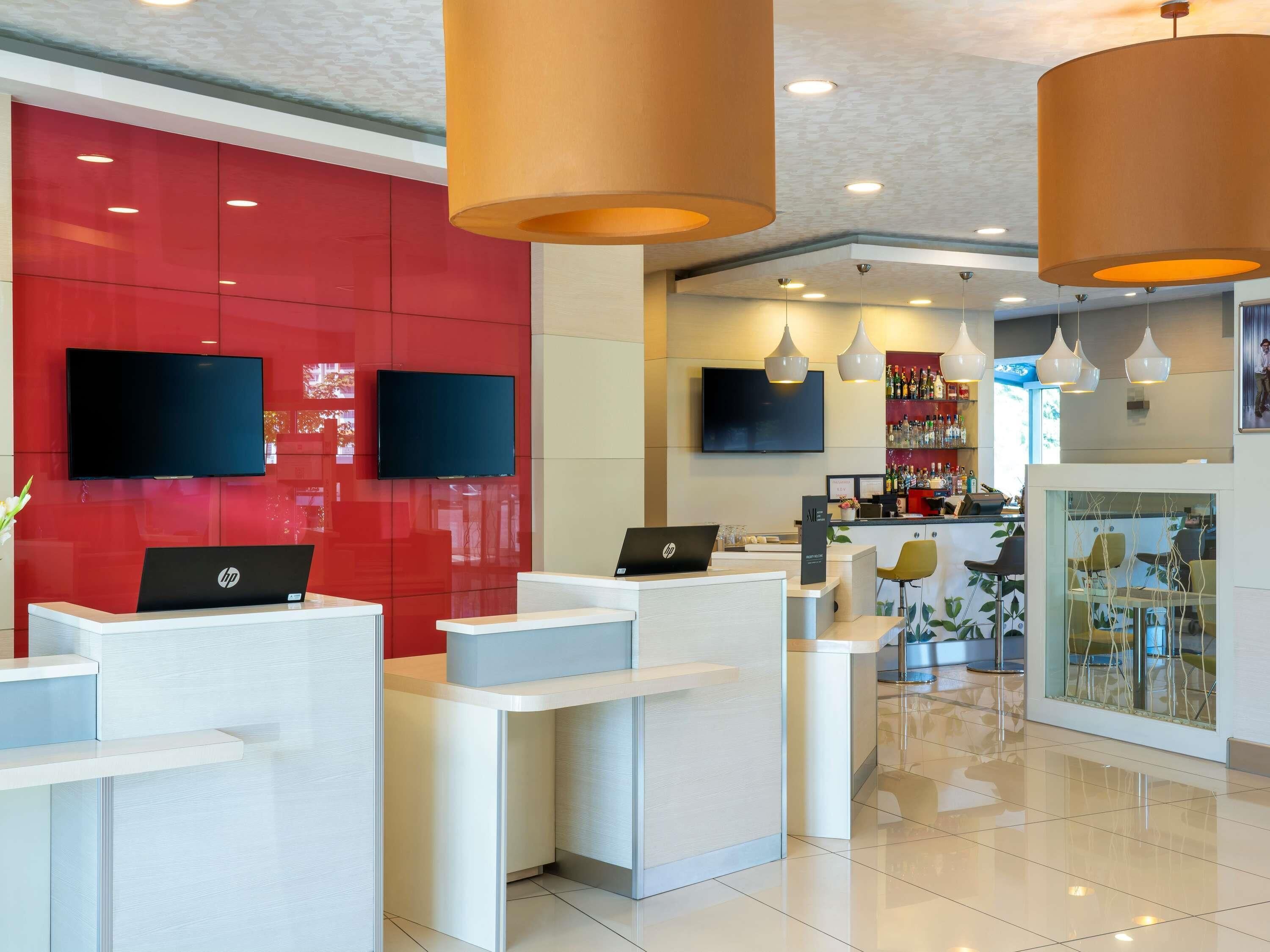 A modern reception area with a red wall, two HP laptops on desks, and a bar area with a glass partition.
