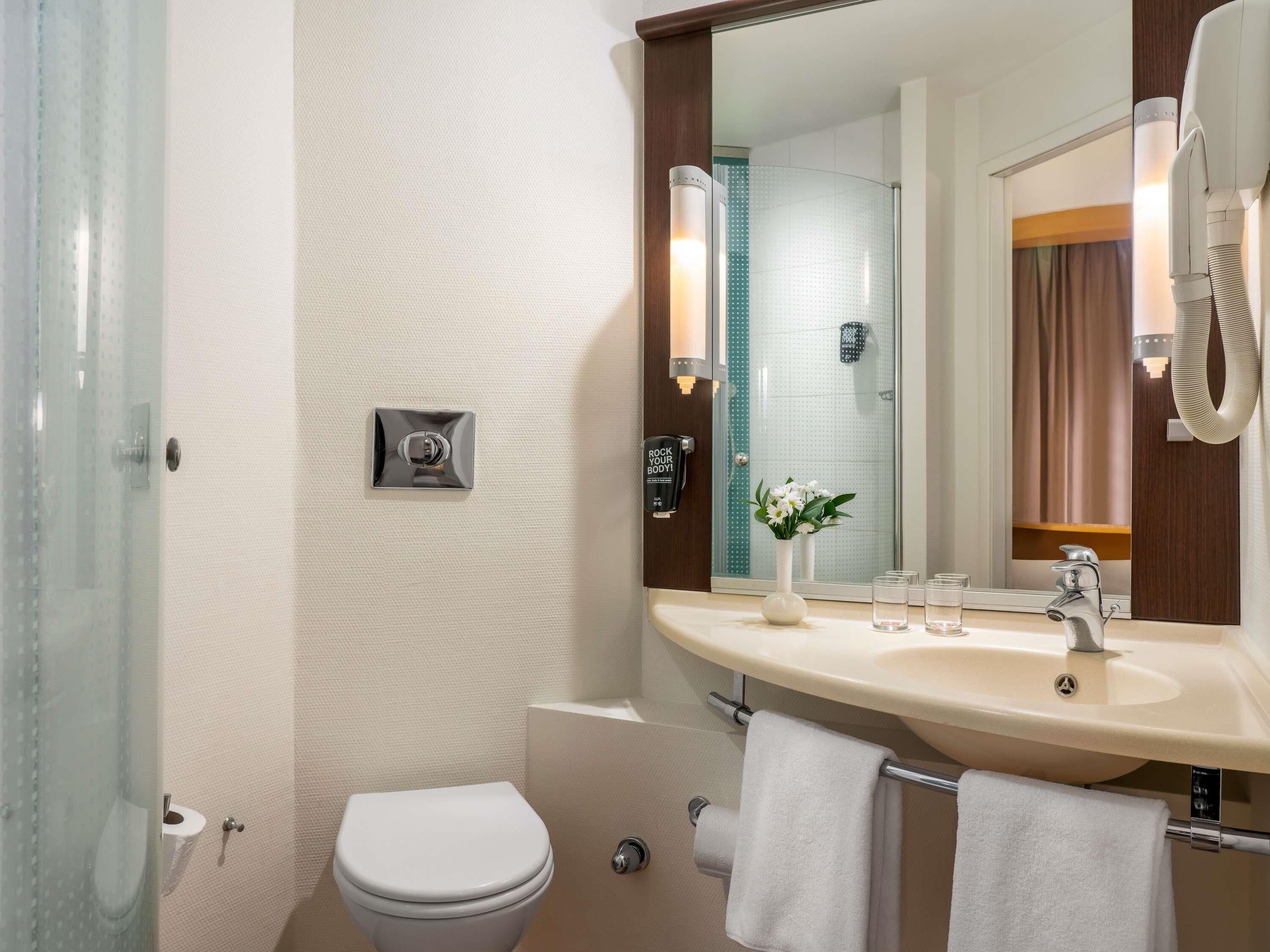 A bathroom with a toilet, sink, mirror, towel rack, and a shower area.