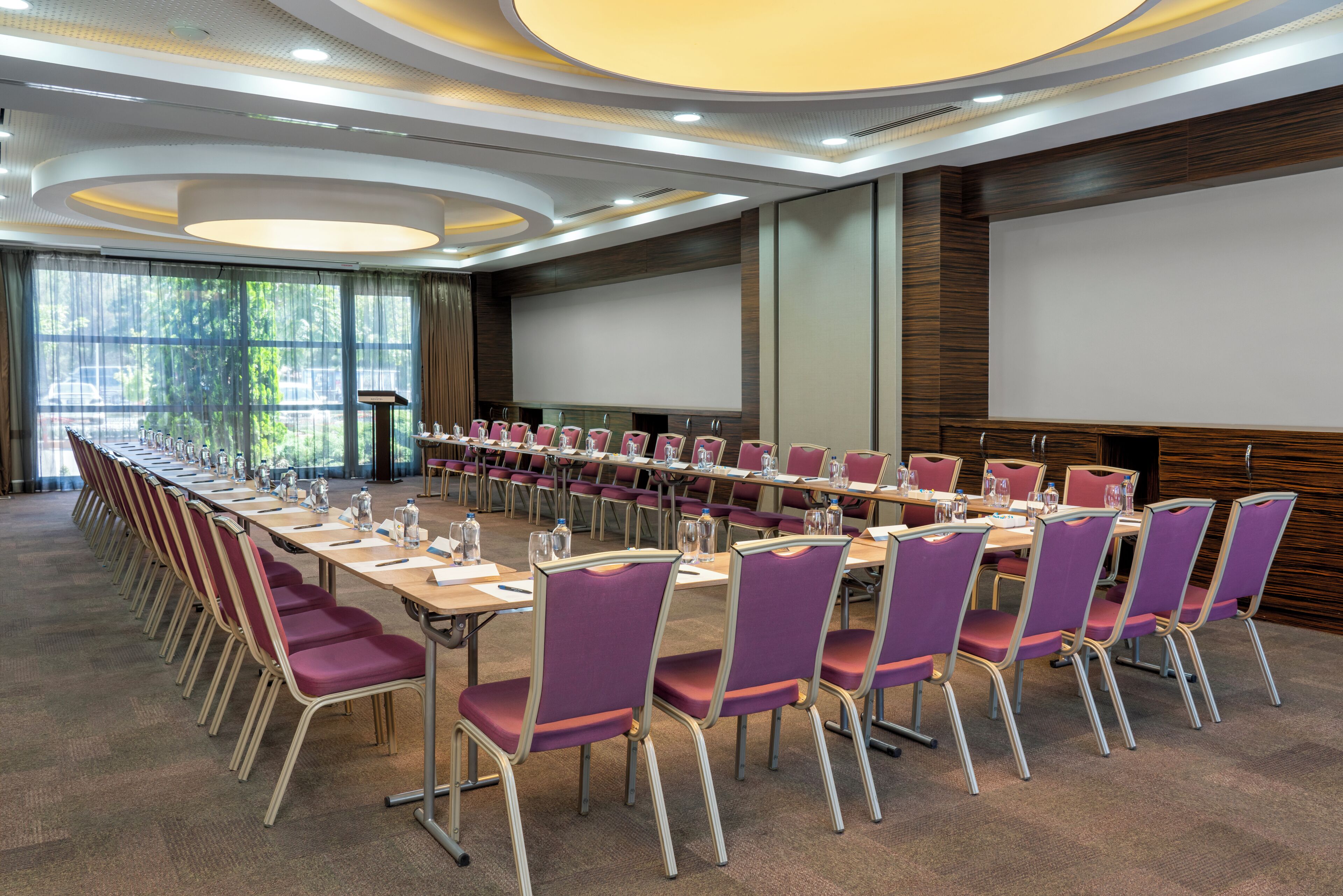 A conference room with a long table, multiple chairs, and a large screen.