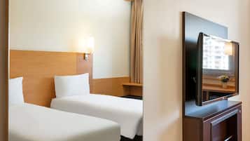 Une chambre d’hôtel avec deux lits, une télévision et une fenêtre donnant sur des immeubles.