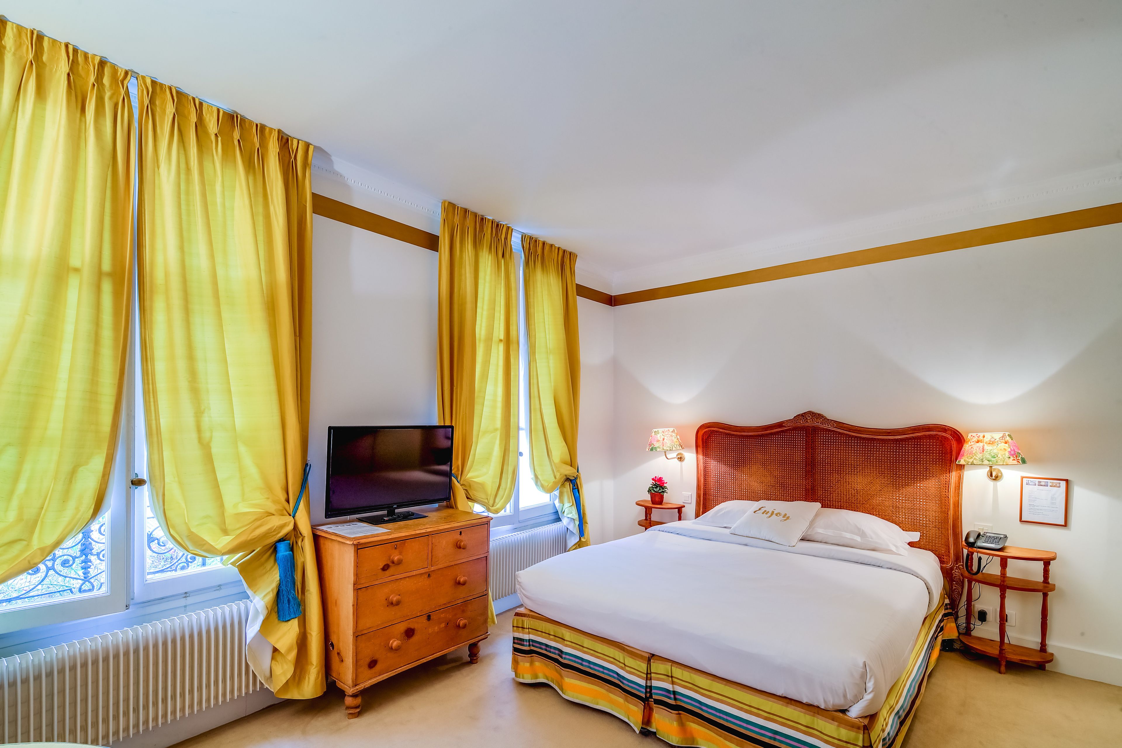 A bedroom with a bed, a TV, a dresser, and a window with curtains.