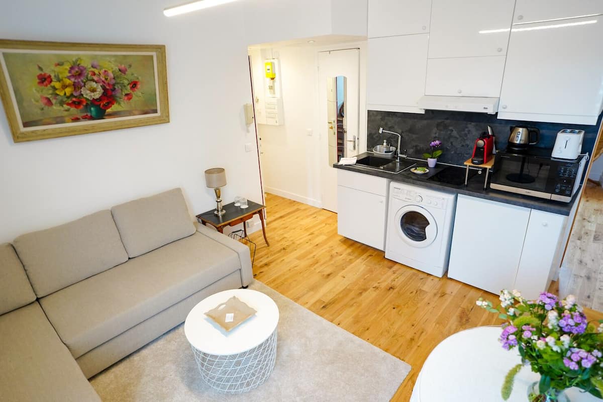 A compact living space with a sofa, a round coffee table, a washing machine, a microwave, and a sink in the kitchen area.