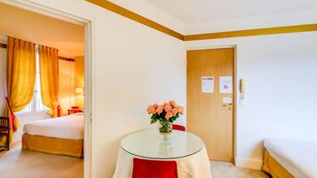Ett hotellrum med en säng, ett litet bord med en vas med blommor, en dörr med en skylt och ett fönster med gardiner.