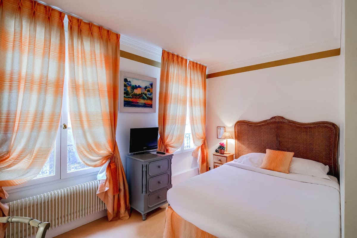 A hotel room with a bed, a dresser, a television, and curtains.
