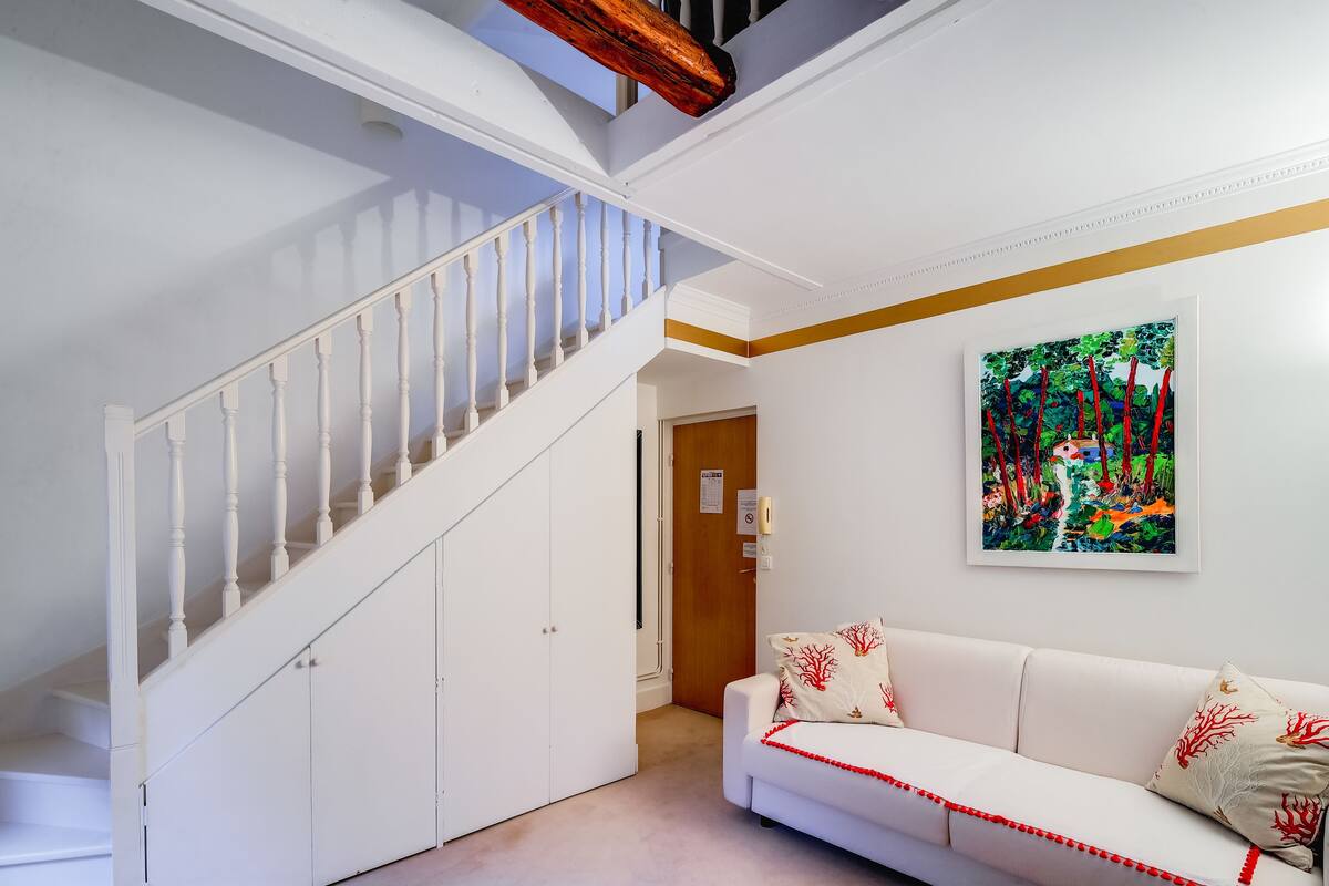A staircase with white railings and a white wall with a framed painting.