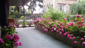 Un sendero bordeado de flores rosas vibrantes, que conduce a un edificio con fachada de piedra y un balcón.