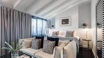 Una habitación de hotel moderna con un conjunto de sofá, una cama con ropa de cama estampada, una mesita de noche con lámpara y un espejo grande.