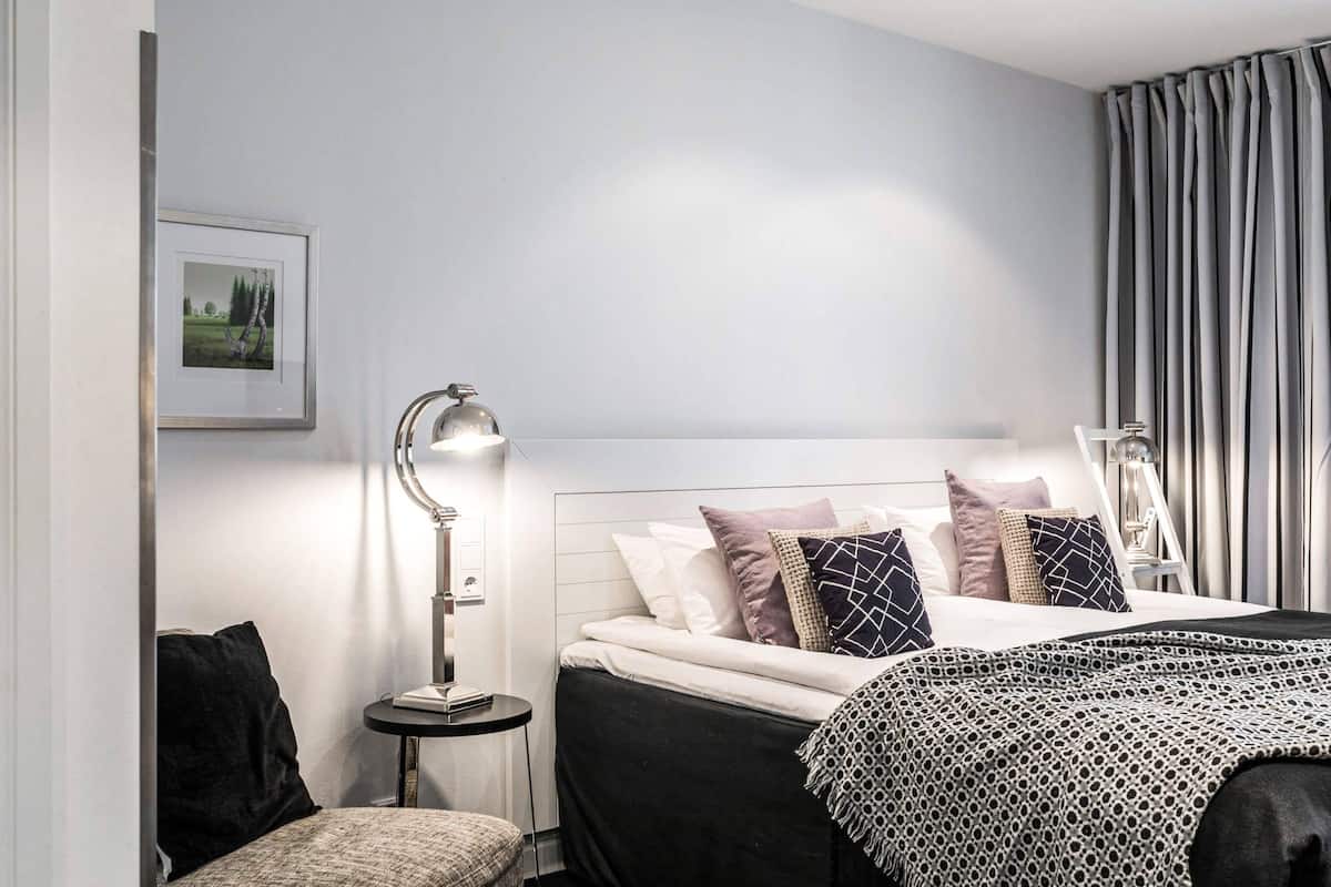 Hotellihuone, jossa on sänky, yöpöytä, lamppu ja seinällä kehystetty kuva.